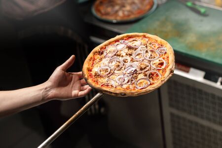 a baker holds pizza on a shovel for baking. top view on hands and pizzaの写真素材