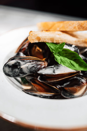 White plate with mussels decorated with a basil on a table in a restaurant . Different focus,...