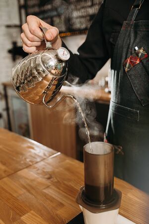 barista preparing coffee in aeropress. barista holding stainless kettle and pouring hot water to aeropressの写真素材