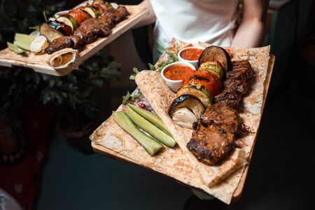 The waiter holds plates with barbecue and grilled vegetablesの写真素材