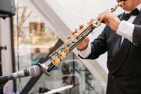 A musician at the event in a frock coat and bow tie plays the saxophone. Ð¡lose-up of hands and toolsの写真素材