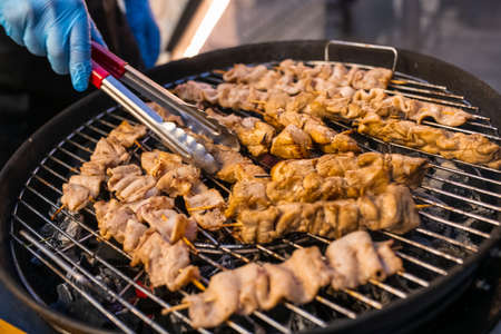Catering banquet outdoors. A chef with gloves prepares barbecue on skewers. Hands and meat close upの写真素材