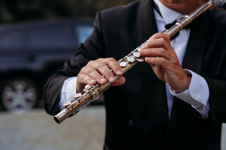 A musician at the event in a frock coat and bow tie plays the flute. Ð¡lose-up of hands and tools