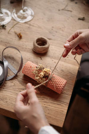 DIY wax candle making process. Woman making decorative wax candle and decorates with dried flowers, close-up of handsの写真素材
