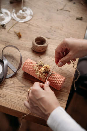 DIY wax candle making process. Woman making decorative wax candle and decorates with dried flowers, close-up of handsの写真素材