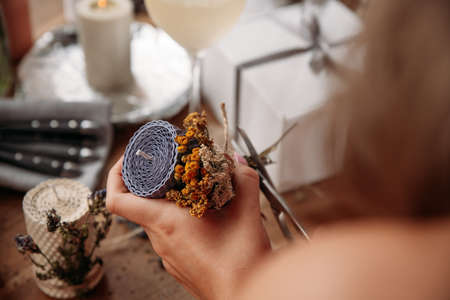 DIY wax candle making process. Woman making decorative wax candle and decorates with dried flowers, close-up of handsの写真素材