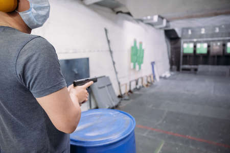 Living in a pandemic. A man in a medical mask aims at a target with a gun at a shooting range amid a pandemicの写真素材