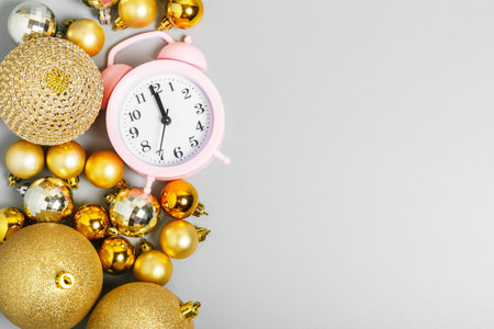  pink alarm clock and golden christmas balls on gray background. Christmas celebration concept. top...
