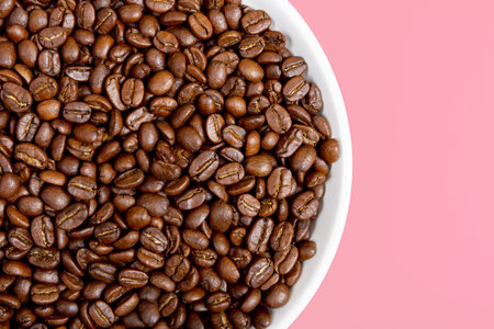 Fragrant coffee beans on a white plate on a pink background. Beautiful background and texture....