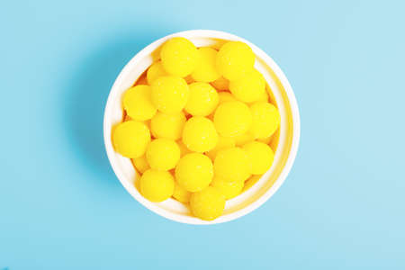 Yellow round candies in a white bowl on a blue background. concept of unhealthy food with sugar. sweets concept for kids. sweets store concept. top view, minimalism.の写真素材