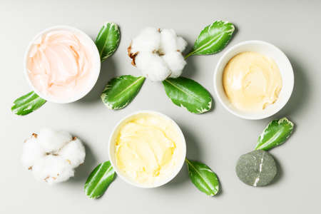 Yellow, pink and beige cream, cotton and green leaves on a gray background. concept of natural cosmetics. top view, flat lay.の写真素材