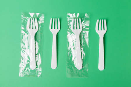 White plastic forks on a green background. The global problem of environmental pollution. flat lay minimalismの写真素材