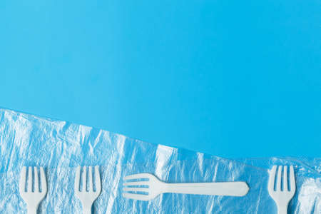 White plastic forks and transparent plastic bag on a blue background. The global problem of environmental pollution. Copy space. flat lay minimalismの写真素材