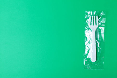 White plastic fork on a green background. The global problem of environmental pollution. Copy space,...