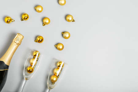 Champagne bottle, champagne glasses and golden Christmas balls lie on a gray background. New Year or Christmas celebration concept. copy space, flat lay, minimalismの写真素材