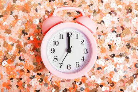 pink alarm clock on a background of pink shiny sequins. New Year or Christmas concept.の写真素材