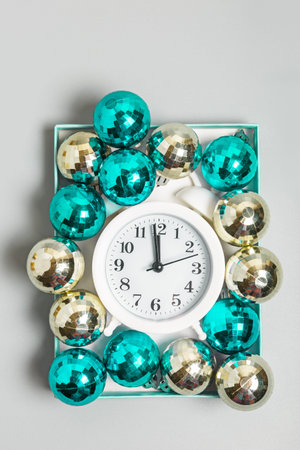 White alarm clock, cyan and silver Christmas balls in a box on a gray background. Christmas or New...
