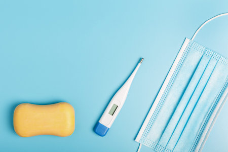 electric thermometer, soap and surgical medical mask on a blue background. concept of protection...