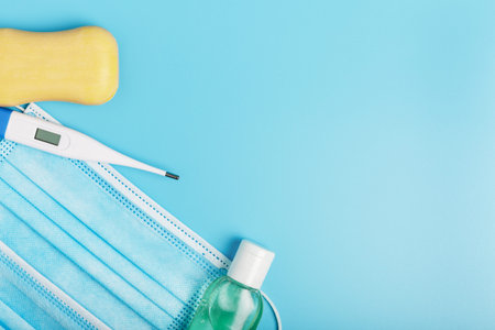 electric thermometer, soap and surgical medical mask on a blue background. concept of protection...
