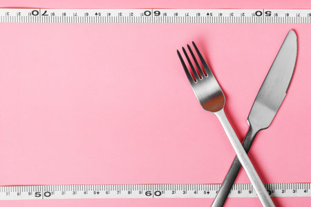 fork, knife and measuring tape on a pink background. The concept of healthy food and diet. Copy spase.の写真素材