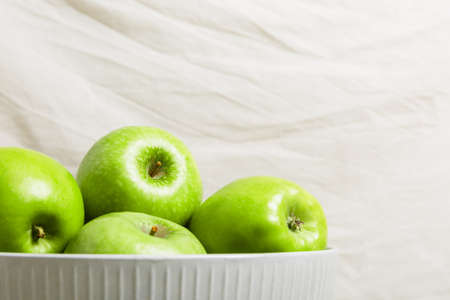 Green apples in a bowl on a light fabric background. Harvest apples, summer season, fresh fruits. copy space.の写真素材