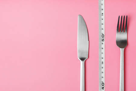 fork, knife and measuring tape on a pink background. The concept of healthy food and diet. Copy spase.の写真素材