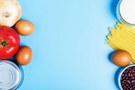 Eggs, rice, beans, pasta, canned food, vegetables on a blue background. Concept of food delivery and food donation during quarantine, coronavirus pandemic. online grocery shopping. copy spaceの写真素材