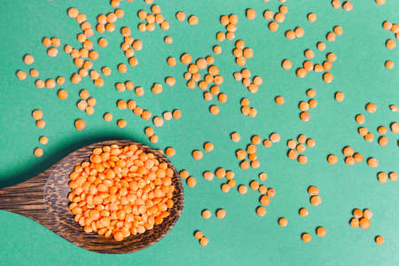 Red lentils in a wooden spoon on a green background. Healthy food concept. Copy spaceの写真素材