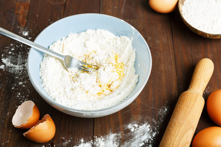 Homemade pasta step by step cooking process. Mixture of flour and eggs in a blue bowl on a wooden...