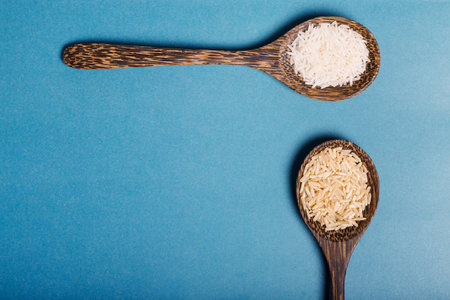 White and brown rice in a wooden spoons on a blue background. Healthy food concept. Copy spaceの写真素材