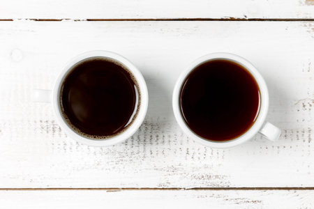 Two mugs of black coffee or espresso on a white wooden table background. The concept of caffeine in...