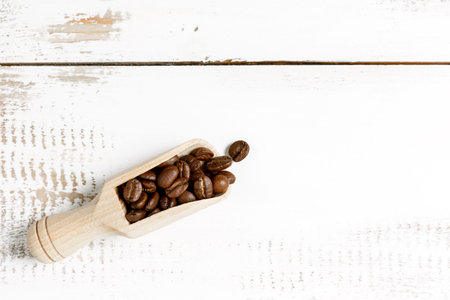 Coffee beans in a wooden spoon on a white wooden table background. Coffee shop or store concept. Awakening morning coffee concept. Copy space, minimalism, top view.の写真素材