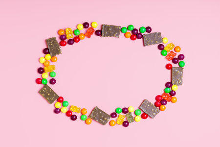 Frame of pieces of chocolate, jelly bears and round candies on a pink background. sweets concept for...