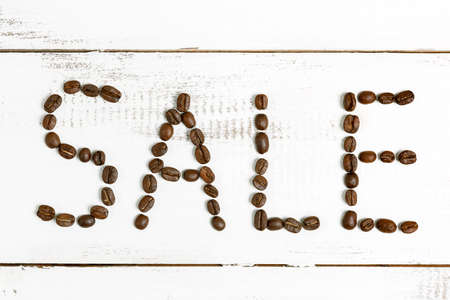 The word sale made of coffee beans on a white wooden background. concept of seasonal sale in stores. concept of discounts in a cafe.の写真素材