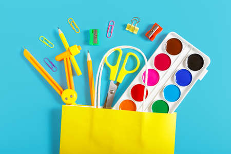 Multi-colored school supplies in a bright yellow paper bag on a blue background. Back to school concept. Concept of shopping in a stationery store. School sale concept. Top view, flat lay.の写真素材