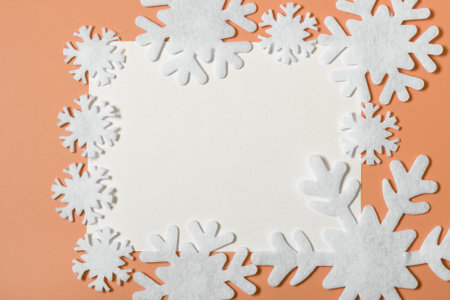 Snowflakes and white blank paper on an orange background. concept of christmas, new year or winter. winter background for designer. copy space, minimalism, flatlay.の写真素材
