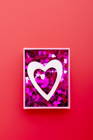 Wooden heart and sequins in a gift box on a red background. The concept of Valentine's day, love, dating and wedding. Symbol of a romantic gift or marriage proposal. Vertical photo.の写真素材