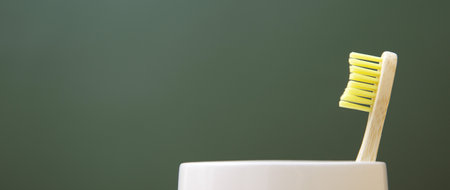 Wooden bamboo toothbrush in a white glass on a green background. The concept of sustainability and the rejection of plastic. The concept of hygiene and daily routine. Copy spase, web bannerの写真素材