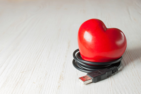 red valentine heart with usb cable on wooden white surfaceの写真素材