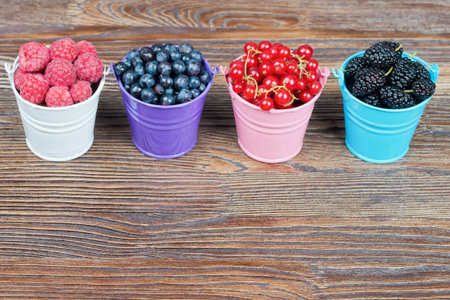 Mixture of berries in little colorful buckets on brown wooden tableの写真素材