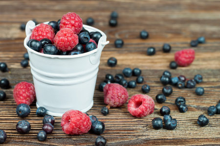 mixed berries in a small bucket on brown wooden background