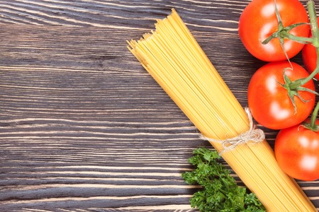 Food ingredients. Pasta spaghetti with tomatoes on brown wooden background. Top view.の写真素材