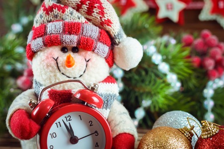 New Year and Chrismas Snowman with a clock on the background of the Christmas tree . Filtered in warm toneの写真素材