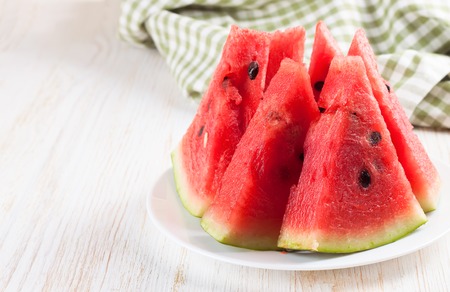 slices of watermelon on the plate on white wooden background with fork and green checkered towel.の写真素材