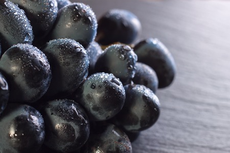 fresh ripe black grapes with drops of water on dark slate background, closeup macro.の写真素材
