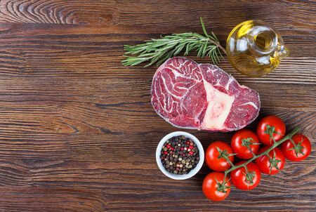 Fresh raw meat beef steak with bone with spices, rosemary, tomatoes and olive oil on wooden background. cooking ingredients. Top view. Flat lay.の写真素材