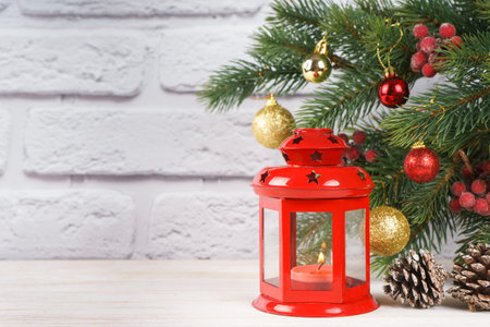 Christmas tree and decorative lantern with a candle. Red retro lantern, cone and balls and fir spruce branches on white brick background with copy space.の写真素材
