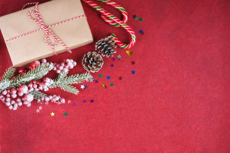 New year background with christmas tree branch, candy, fir cones and gift box on red felt background with space for text. Flat lay, top view.の写真素材