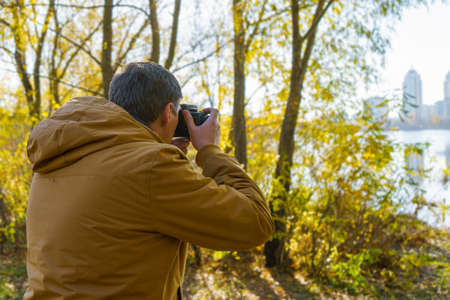Professional male photographer shooting outdoor in fall yellow forest on modern dslr camera. Empty area with copy space for text.の写真素材