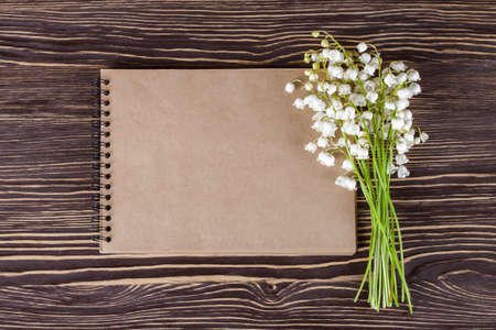 Bouquet of flowers lily of the valley and empty paper notebook on brown rustic table.の写真素材